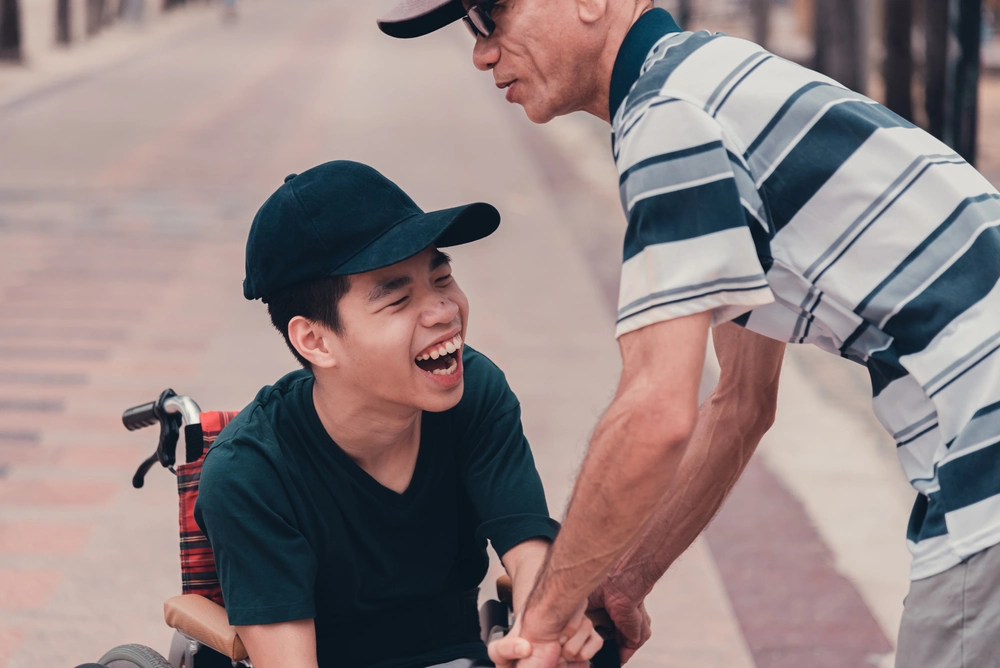 down syndrome boy on wheel chair smiling with his caretaker